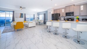 Une cuisine moderne dotée d’un îlot central, de tabourets de bar et d’un coin repas avec un canapé blanc et un fauteuil jaune.