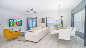 Un salon moderne avec un canapé blanc, un fauteuil jaune et un coin repas comprenant des chaises et une table, le tout dans des tons blancs.