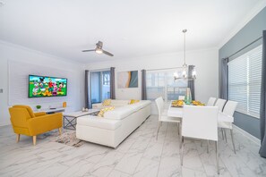 Relax in this stylish living room with a sofa, armchair, and dining area, featuring a flat-screen TV and ceiling fan.