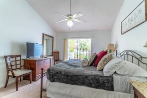 Une chambre à coucher comprenant un lit, un bureau, une chaise, un ventilateur de plafond et une fenêtre.