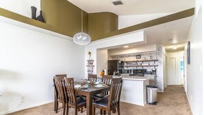 Un coin repas avec une table dressée pour quatre personnes, des chaises en bois et un luminaire suspendu.