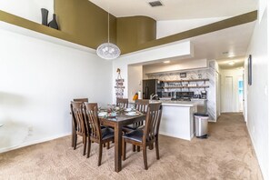 A modern dining area with a wooden table and chairs, a hanging light fixture, and a kitchen in the background. - New Listing! Royal Palm Bay Resort, 5mi to Disney & 10mi to Universal - IT9921 (Kissimmee)