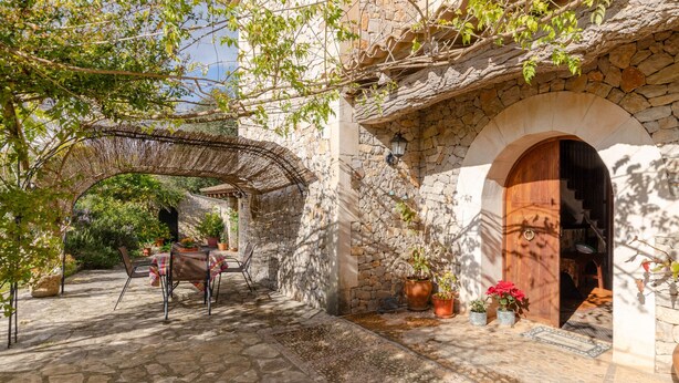 Ein steinerner Innenhof mit einer rustikalen Holztür, einer gewebten Pergola und Topfpflanzen.