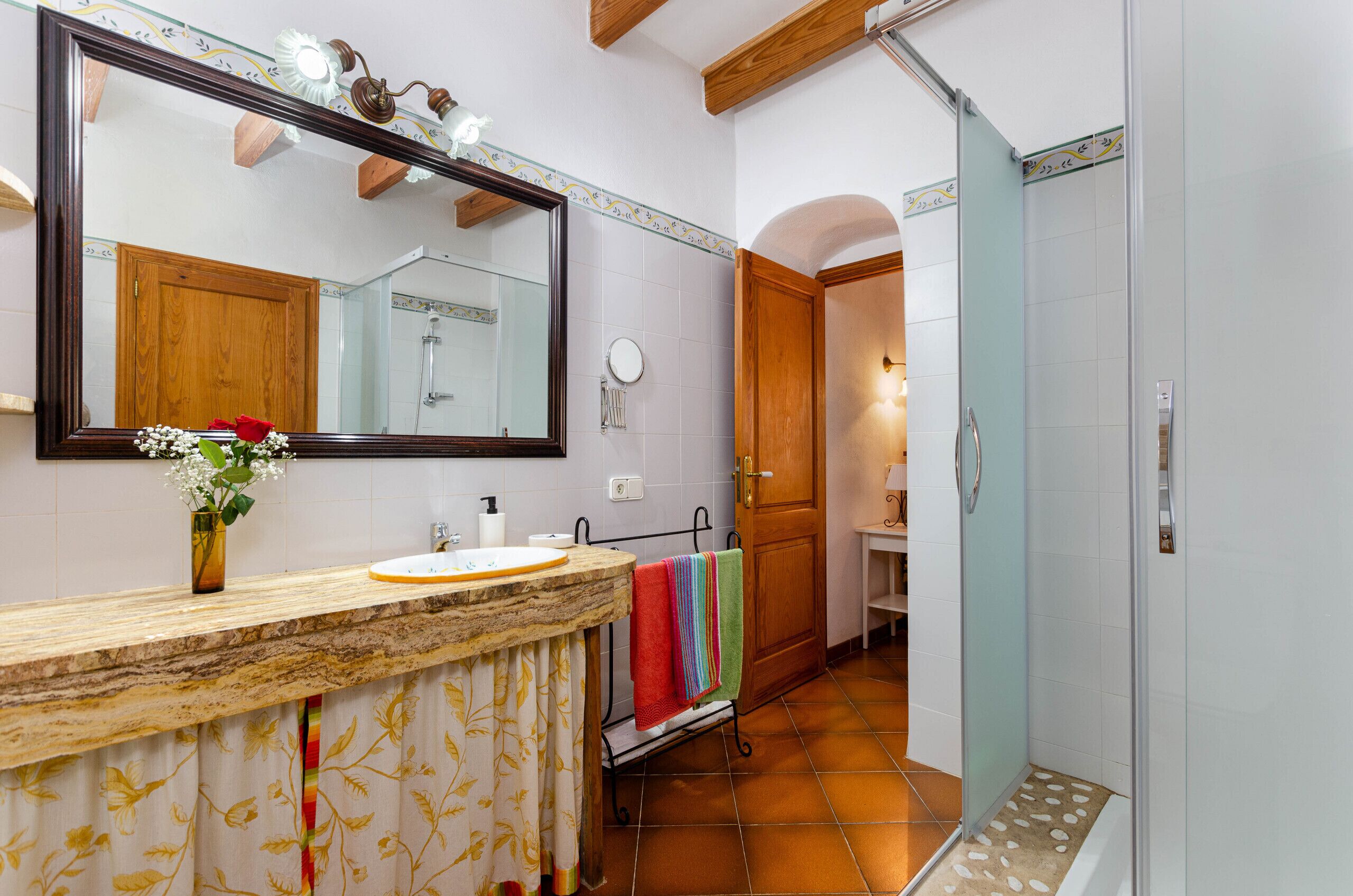 A bathroom with a large mirror, a sink, a shower, and a towel rack.