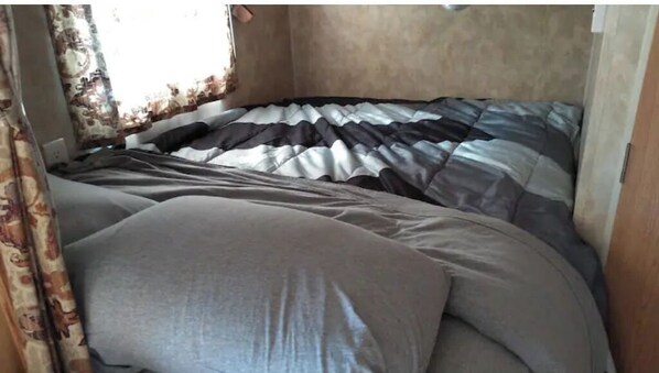 Una cama con una colcha a rayas y un almohadón gris en una habitación con ventana y cortinas.