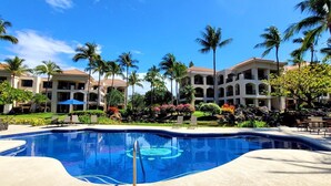A resort with a swimming pool, palm trees, and a multi-story building with balconies.