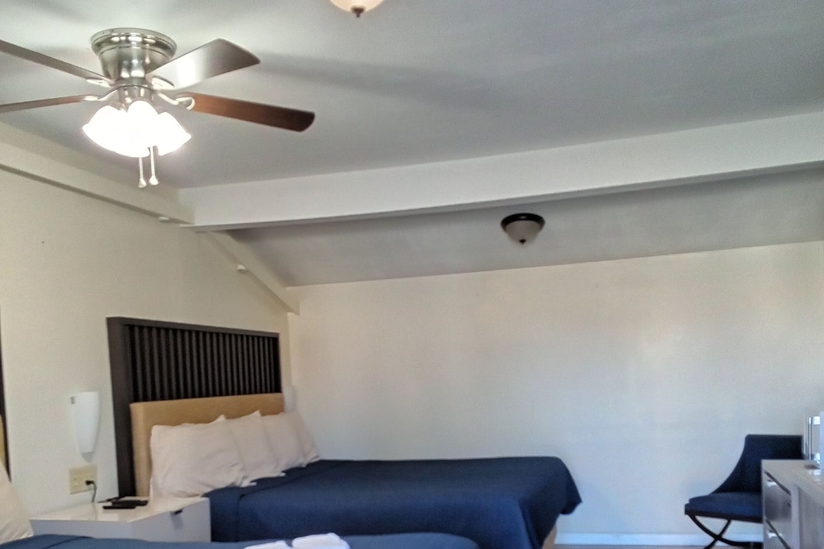 A hotel room with two beds, a ceiling fan, a desk, and a chair.