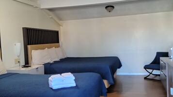 A hotel room with two beds, a ceiling fan, a desk, and a chair.