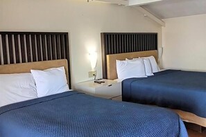 A hotel room with two beds, each with a headboard and pillows.