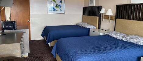 Quarto de hotel com duas camas, uma mesa de trabalho e um abajur fixado na parede.
