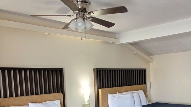 A hotel room with two beds, a ceiling fan, a nightstand with a lamp, and a wooden floor. - Howard Johnson by Wyndham Sebring (Sebring)