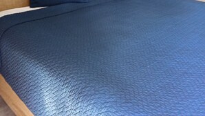 A neatly made bed with a blue bedspread and pillows, a wooden headboard, a wall-mounted light, and a framed picture above the headboard. - Howard Johnson by Wyndham Sebring (Sebring)