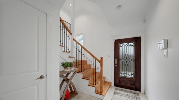 A clean, modern hallway with a wooden staircase, a decorative door, and a marble floor.