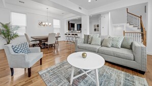 A spacious living room with a grey sofa, a round white coffee table, and a dining area with a wooden table and chairs.