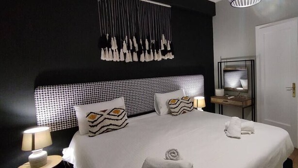 Quarto de hotel moderno com uma cama grande, mesa de cabeceira com luminária, espelho e guarda-roupa.