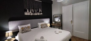 Et moderne hotelværelse med en stor seng, et natbord med lampe, et spejl og et garderobeskab.