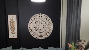 Uma sala de estar com sofá, mesa de centro, mesa lateral, luminária pendente e arte decorativa na parede.