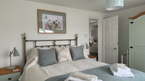 A neatly made bed with a floral print headboard, a bedside lamp, and a framed picture above it.