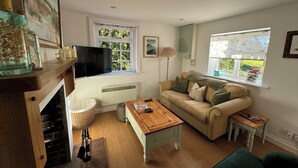 A cozy living room with a sofa, a wooden coffee table, a television mounted on the wall, and a fireplace.