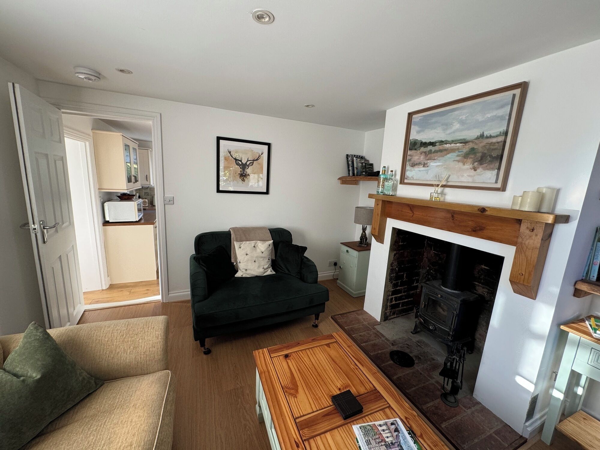 A living room with a fireplace, a sofa, a coffee table, and a kitchen visible through an open door.