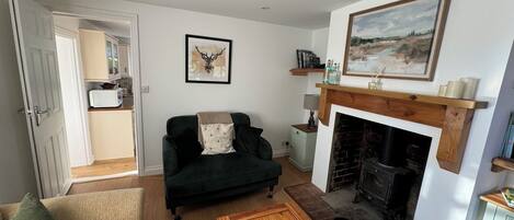 A living room with a fireplace, a sofa, a coffee table, and a kitchen visible through an open door.