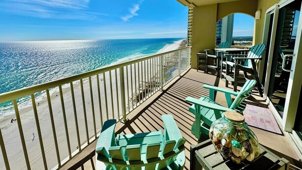 Een balkon met uitzicht op het strand en de oceaan. Er staan groene stoelen en een tafel op het balkon.