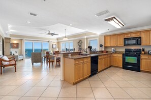 Cozinha espaçosa com armários de madeira, micro-ondas preto e lava-louças. Há um espaço de jantar com mesa e cadeiras, e um ventilador de teto.