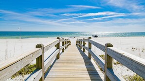 Een houten looppad naar een strand met een helderblauwe lucht.