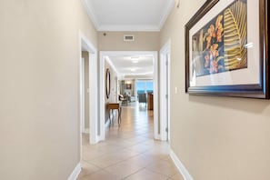 Um corredor com piso de azulejos, obras de arte nas paredes e vista para uma sala de jantar com mesa e cadeiras.