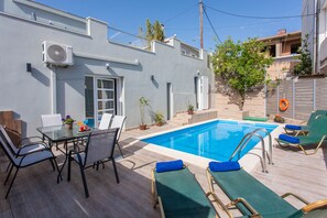 A swimming pool area with lounge chairs and a table with chairs and a potted plant.