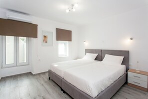 A modern bedroom with a large bed, a bedside table, and a window with blinds.