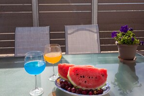 A table with a glass of blue liquid, a glass of orange liquid, watermelon slices, and a plate with grapes.