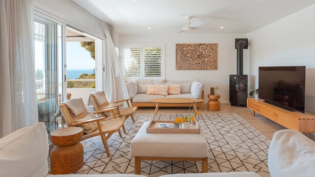 A modern living room with a sofa, chairs, a TV, and a fireplace. - Feel The Aroha-Love At This Beautiful Beach Haven (MACMASTERS BEACH)