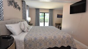 Ein Schlafzimmer mit einem großen Bett, einem Nachttisch, einem an der Wand montierten Fernseher und einem Fenster mit Vorhängen.