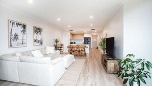 A modern living room with a sofa, a dining area with wooden chairs, a kitchen with wooden cabinets, and a flat-screen TV on a wooden stand. - Casa del Navilla - Experience luxurious living right on Ulladulla Harbour (Ulladulla)