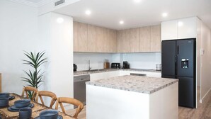 A modern kitchen with light wood cabinets, a black refrigerator, and a granite countertop. - Casa del Navilla - Experience luxurious living right on Ulladulla Harbour (Ulladulla)