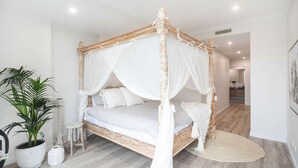 A four-poster bed with white bedding, a potted plant, and a small stool. - Casa del Navilla - Experience luxurious living right on Ulladulla Harbour (Ulladulla)