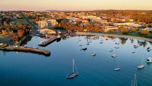 A marina with numerous boats docked, surrounded by a town with buildings and a hilly landscape in the background. - Casa del Navilla - Experience luxurious living right on Ulladulla Harbour (Ulladulla)