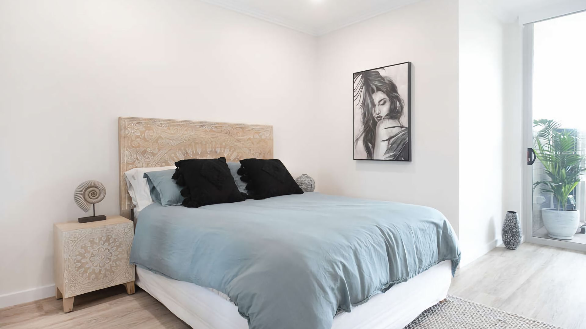 A bedroom with a bed, a nightstand, a wall art piece, and a potted plant.