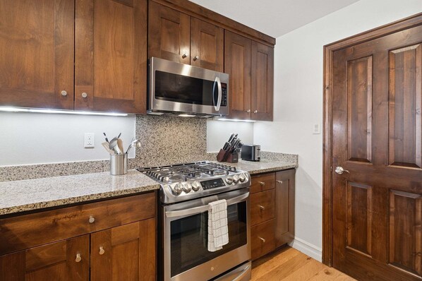 A kitchen with wooden cabinets, a stainless steel microwave, a gas stove, and granite countertops.