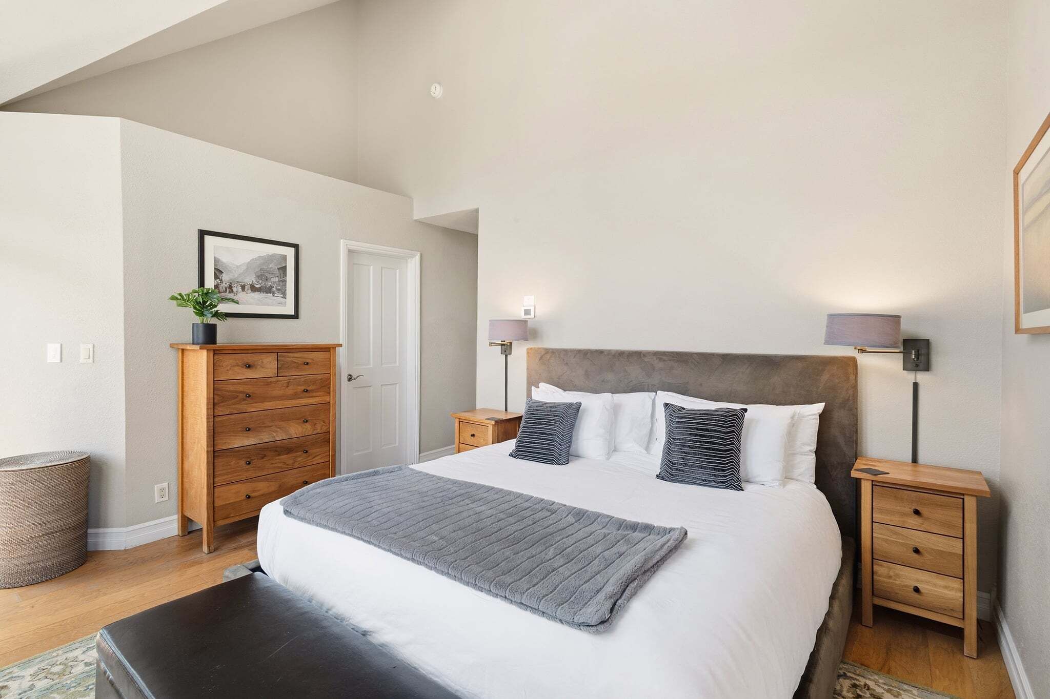 Une chambre à coucher avec un grand lit, des tables de chevet, une commode, un tableau encadré au mur et une lampe.