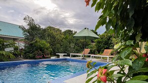 Piscina con azulejos azules, rodeada de follaje y un cielo nublado.