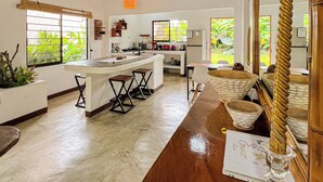 Una cocina amplia con techo de madera, una isla central con taburetes y vista a zonas verdes.