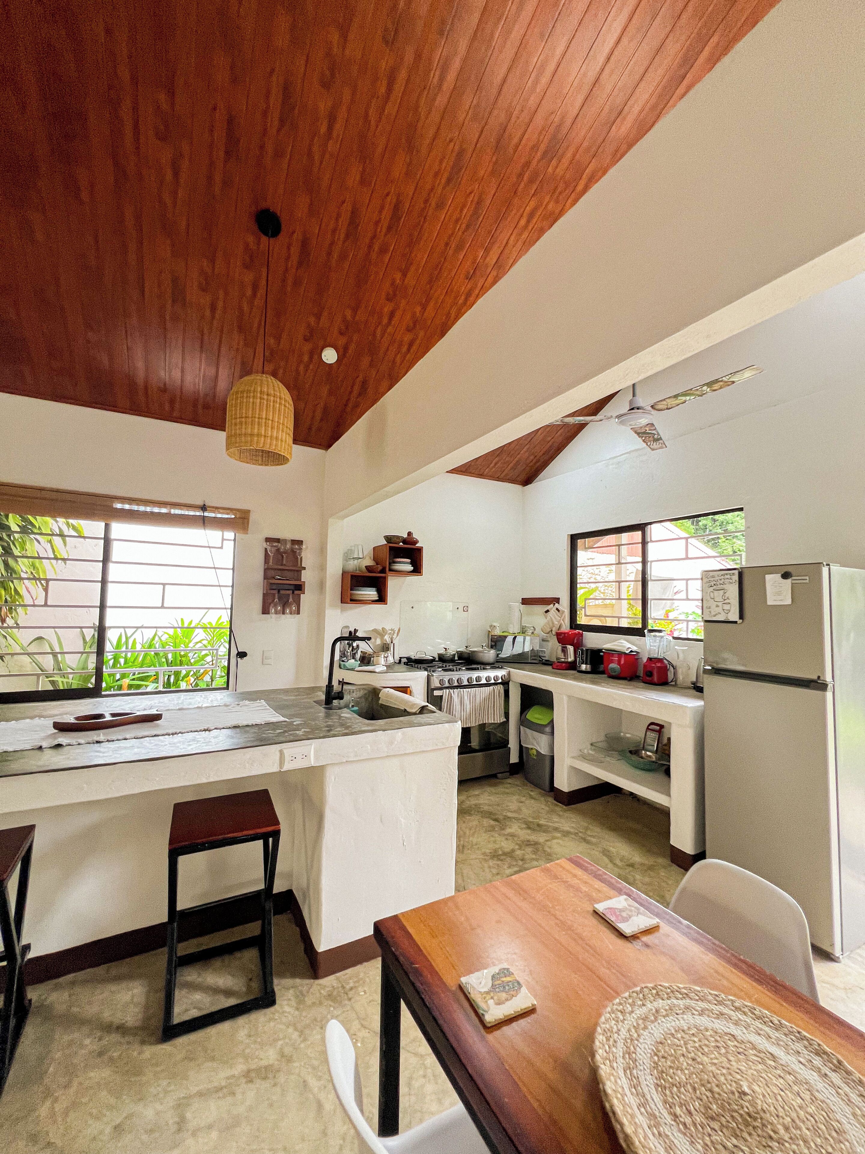 Une cuisine spacieuse avec un plafond en bois, un grand îlot central doté d’un évier et un coin repas avec une table et des chaises.