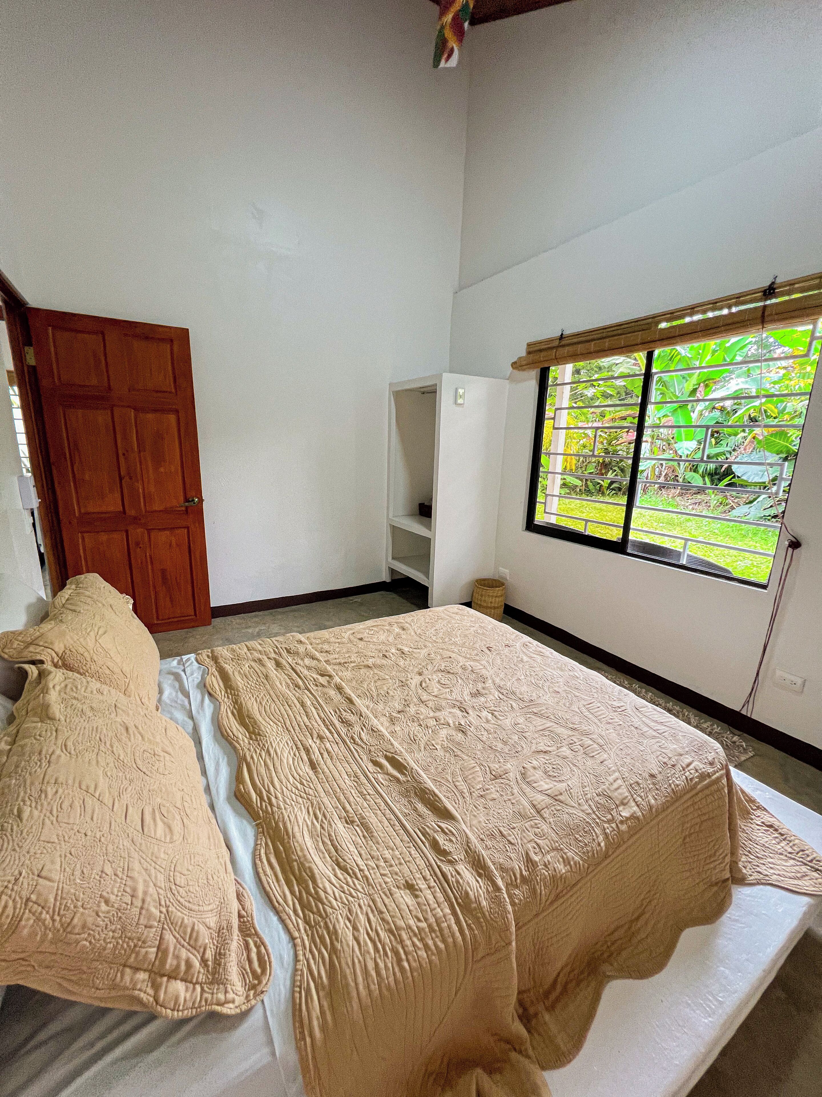 Un dormitorio con cama, armario, ventana con vistas a vegetación y estantería.