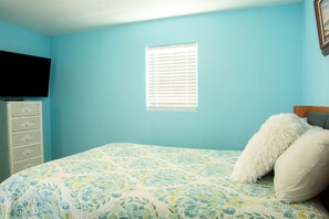 Un dormitorio con cama, cómoda, ventana y televisor en la pared.
