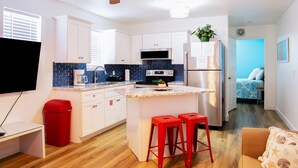 A compact kitchen with white cabinets, a blue backsplash, a stainless steel refrigerator, and a ceiling fan.