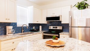 A kitchen with white cabinets, a stainless steel refrigerator, a microwave, an oven, and a coffee maker.