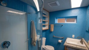 Un baño con cabina de ducha de vidrio, inodoro, lavabo con encimera de mármol y pared azul.