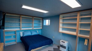 Un dormitorio con cama, estanterías empotradas, ventana y aire acondicionado.